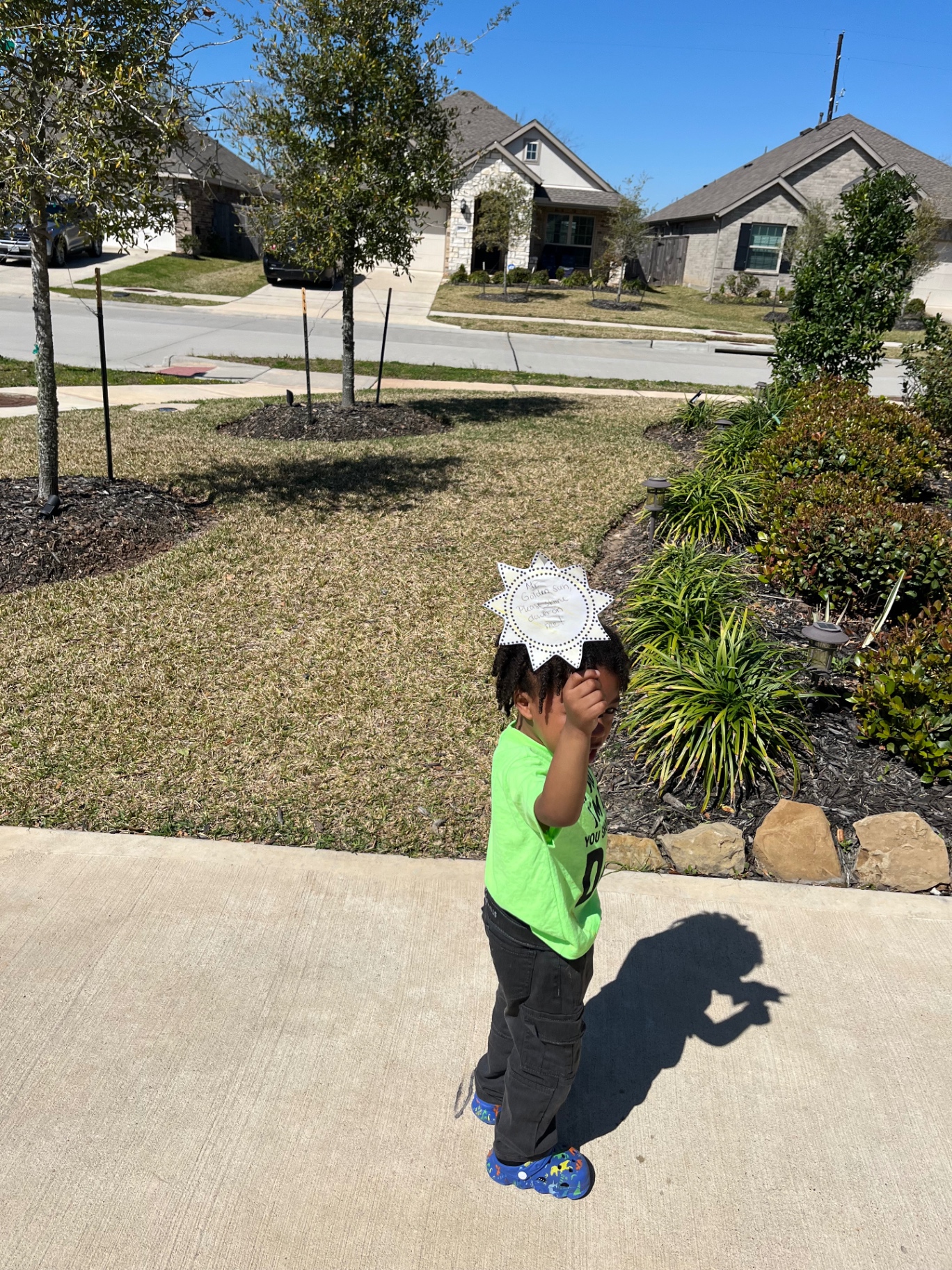 A child outside wearing a handmade paper sun craft on a sunny summer day