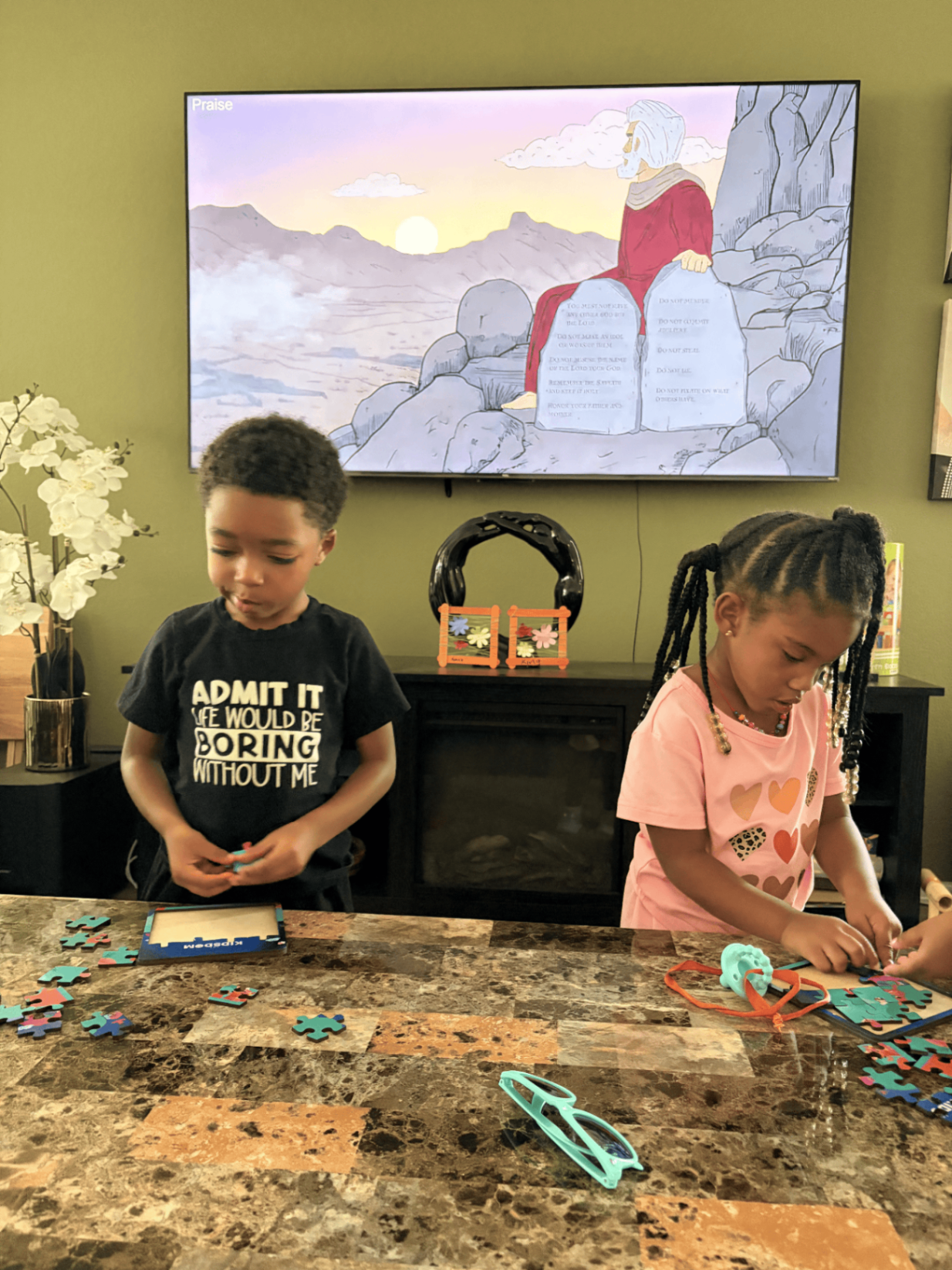 Two preschoolers building Bible story puzzles while a Ten Commandments lesson plays on screen