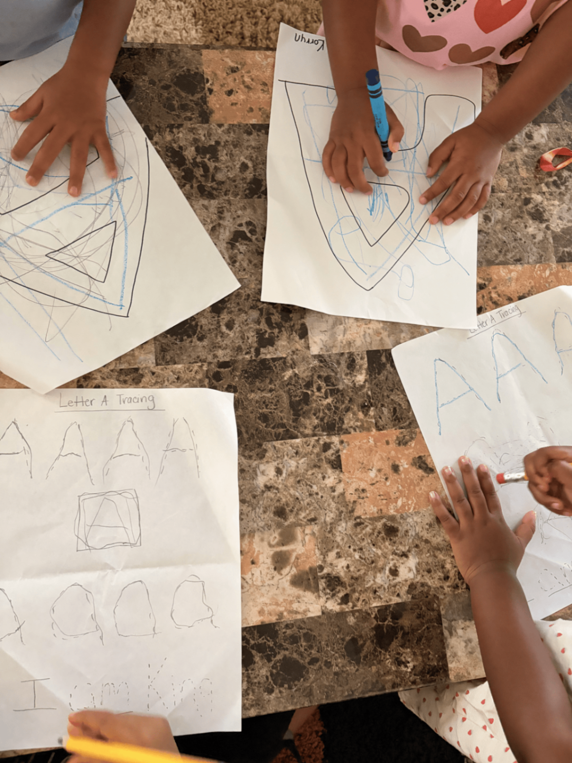 Preschoolers coloring and tracing Letter A handwriting worksheets around the table